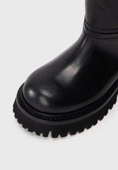 Juodos odinės botai su apvaliu pirštu ir storu guminiais padu, turinčiu dantytą briauną. Lygus paviršius su subtiliomis siūlės detalėmis.
