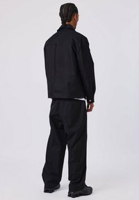 Veste noir surdimensionnée avec un col, des poignets à boutons et un pantalon noir assorti. Le matériau semble lisse, avec une coupe décontractée et un minimum de détails.