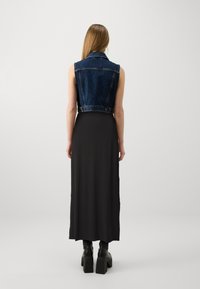 Denimvest med ærmeløs design og cropped snit, parret med en lang sort maxi-kjole, båret med chunky hæle støvler.