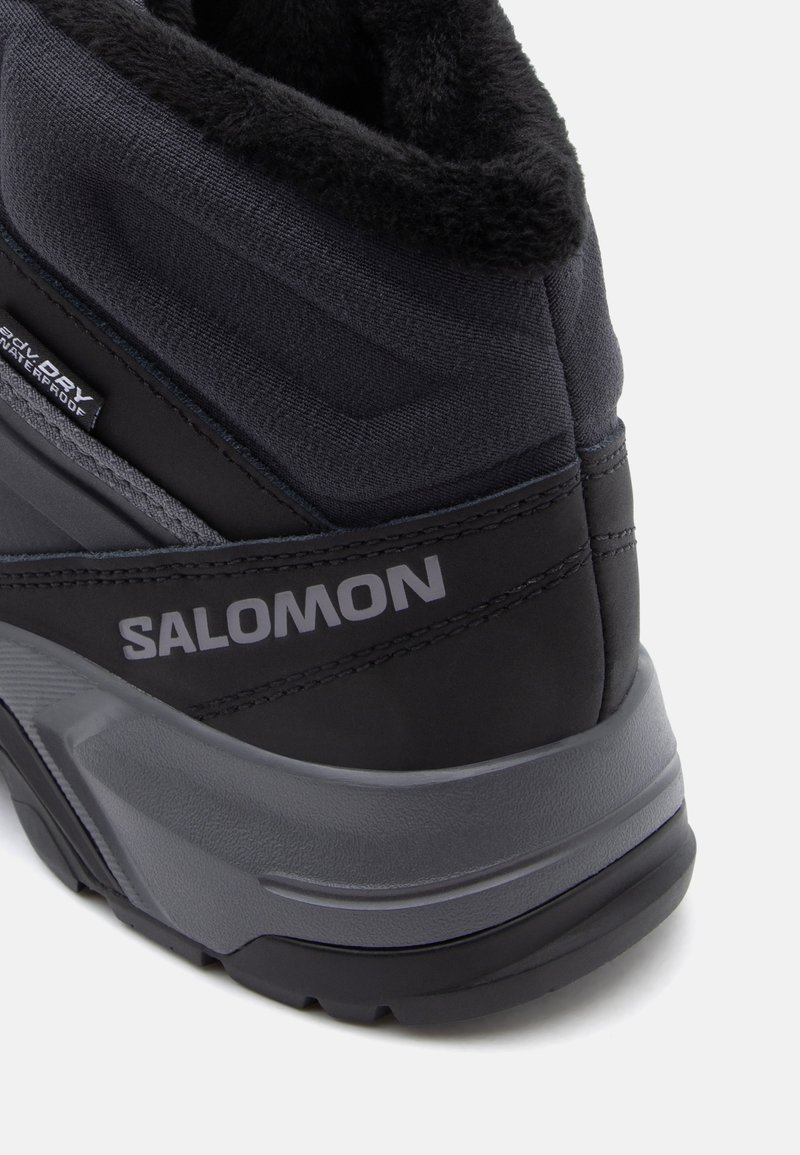 Stivale nero impermeabile con tomaia in tessuto testurizzato, dotato di colletto imbottito e logo grigio dettagliato. Suola rinforzata per la trazione.