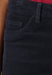 Donker marineblauwe corduroy broek met een textuur ribbelpatroon, een voorzak en een verborgen taillebanddetail.