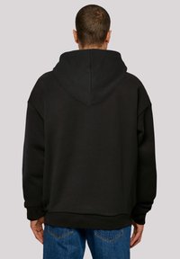 Svart hettegenser med avslappet passform, oversized ermer og teksturert stoff. Bakfra vises sømdetaljer og en stor hette.