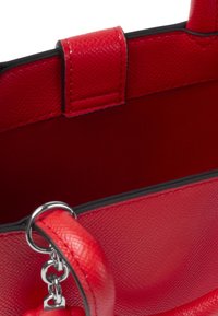 Bolso de mano de cuero rojo con superficie texturizada, ribete negro y herrajes plateados. Presenta un accesorio de mango circular y un interior liso.