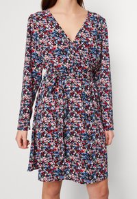 Blommig omlottklänning med långa ärmar, med en v-ringning, bältesdetalj och en mörk marin bakgrund fylld med färgglada blommönster.