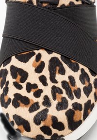 Læderskindsko med leopardmønster, der har en blød, tekstureret overflade med sorte elastiske stropper, der krydser over toppen, afsluttet med en hvid sål.