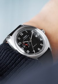 Timex Marlin automatic watch with a black textured face, stainless steel case, white numbers, and a red second hand on a black strap.
