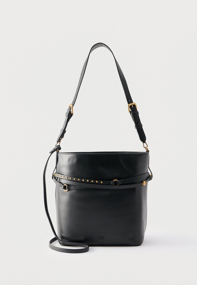 Μαύρη δερμάτινη τσάντα τύπου bucket με ρυθμιζόμενο ιμάντα ώμου, διακοσμητική ζώνη με καρφιά και εξαρτήματα σε χρυσαφί απόχρωση σε απλό λευκό φόντο.