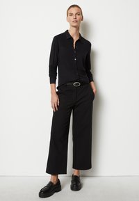 Camisa negra de botones con mangas largas, combinada con pantalones anchos negros. El conjunto incluye un cinturón negro con una hebilla plateada y zapatos negros.