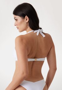 Bikini bianco con collare al collo e fiocco, chiusura dorata sul retro e un tessuto liscio e strutturato.