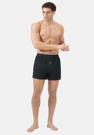 Schwarze Schwimmshorts mit elastischem Bund, vorderem Knopfdetail und lockerer Passform. Glatte Textur und Oberschenkellänge.