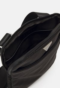 Borsa a tracolla nera con finitura testurizzata, chiusura con zip e tasca interna. Caratterizzata da un'accenno di logo argentato sulla parte anteriore.