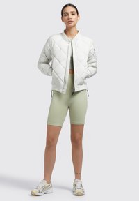 Quilted white bomber jacket with ribbed cuffs, green fitted top, light green bike shorts, and multicolored athletic shoes. Simple background.