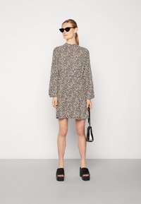 Vestido de padrão de leopardo com mangas longas, gola alta e um corte descontraído. Combinado com saltos altos pretos e uma pequena bolsa preta.