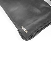 Sort læderhandske med glat tekstur, der har en guldfarvet "maze"-logo nær kanten. Designet er slankt med en tætsiddende form og uden yderligere detaljer.