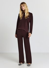 Maglione a maglia bordeaux e pantaloni ampi abbinati; tessuto morbido, vestibilità comoda; scarpe con motivo a serpente. Sfondo minimalista.