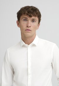 White long-sleeve shirt displayed on a light background. Features button-down collar and smooth fabric texture. No patterns or accents visible.