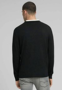 Zwarte trui met lange mouwen en een wit kraagdetail. Geribbelde zoom en manchetten, gladde textuur, standaard pasvorm. Gezien van achteren.