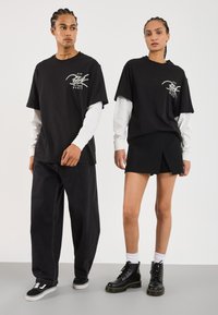 Sorte grafiske t-shirts lagdelt over langærmede hvide skjorter, parret med mørke vide jeans og en sort nederdel, suppleret med sorte støvler.