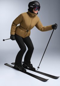 Ski outfit featuring a brown insulated jacket with a high collar and belt, paired with black ski pants, gloves, helmet, and skis.