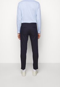 Granatowe spodnie o dopasowanym kroju, gładkiej fakturze, z dwoma tylnymi kieszeniami i dopasowanym fasonie. W połączeniu z jasnoniebieską koszulą z długim rękawem.
