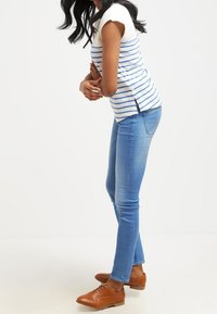 Camiseta a rayas azul y blanca combinada con unos jeans ajustados de color azul claro y zapatos de cuero marrón, creando un look casual y relajado.