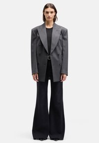 Grijze dubbelgeknoopte blazer met brede revers, zwarte knopen en een gestructureerde afwerking, gecombineerd met zwarte uitlopende jeans en een aansluitend zwart topje.