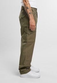 Pantalones cargo verde oliva hechos de una duradera tela de algodón, con bolsillos laterales, un corte recto y combinados con zapatillas blancas.