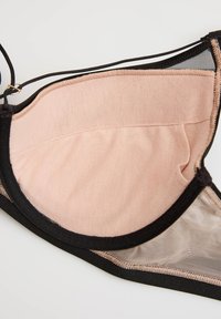 Jemnoružová košíček podprsenky s čiernym lemovaním a nastaviteľným tenkým čiernym ramienkom na jednoduchom svetlom pozadí.