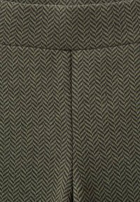 Tissu à motif pied-de-poule en vert foncé et noir. Texture lisse avec un léger étirement. Présente un design taille haute.