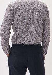 Camicia a fantasia multicolore con colletto a bottoni e maniche lunghe, realizzata in tessuto leggero, abbinata a pantaloni di colore scuro.