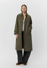 Olíva zöld, laza szabású, hosszú kabát, galléros nyakkal, gombos záródással és oldalsó zsebekkel. Sötét, bő szárú farmernadrággal párosítva.