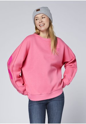 Rosa Sweatshirt mit gerippten Bündchen und Kragen, mit einem Logo auf der Brust und grafischen Akzenten an den Ärmeln. Kombiniert mit einer grauen, gestrickten Mütze.