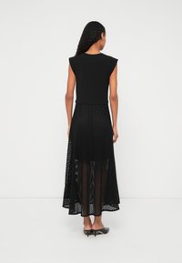 Čierne šaty s priliehavým vrškom a prúdiacou, priesvitnou sieťovanou sukňou. Dizajn obsahuje krátke rukávy a dlhú, viacvrstvovú siluetu.