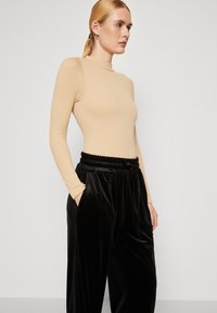 Beige langermet body med høy hals, kombinert med svarte fløyelsbukser med elastisk midje og sidelommer.