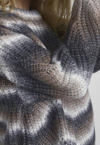 Maglione a maglia in tonalità di grigio, marrone e crema. Presenta un motivo testurizzato con strisce ondulate e una vestibilità accogliente.