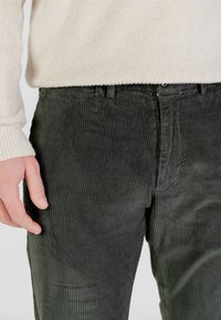Pantaloni in velluto a coste verde scuro con righe verticali, dotati di chiusura con bottoni, passanti per cintura e tessuto strutturato.