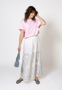 Lys rosa t-skjorte med korte ermer paret med en hvit, blonde maxi-skjørt med blomsterutskjæringer. Brukt med blå sklisandaler og en denim-veske.