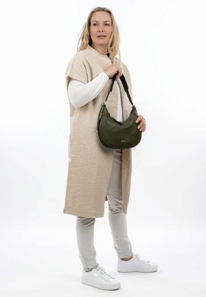 Borsa in pelle verde oliva con una forma curva e una tracolla, tenuta da una persona in un cappotto beige morbido, camicia bianca a maniche lunghe e pantaloni chiari.