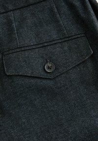 Dark denim fabric features a patch pocket with a pointed flap and a single black button closure, showcasing a textured surface.