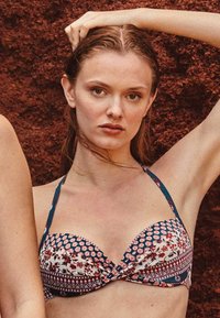 Top bikini multicolore con motivi floreali e geometrici, coppe imbottite e sottili spalline regolabili, caratterizzato da un design anteriore attorcigliato.