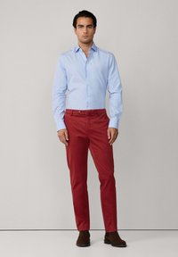 Camisa de botón a rayas azul claro y pantalones chinos rojos lisos, combinados con botas de tobillo marrón oscuro. El tejido parece suave y bien confeccionado.