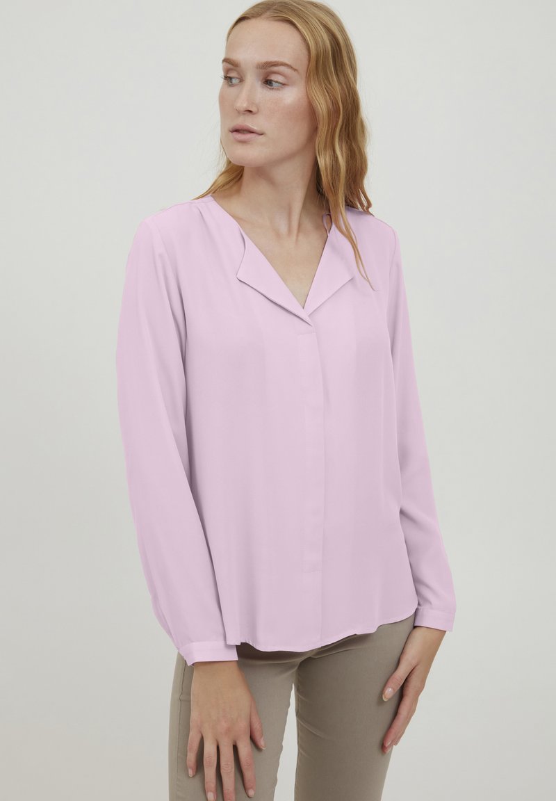 Blusa rosa chiaro a maniche lunghe con abbottonatura frontale, orlo curvo e colletto. Tessuto liscio, vestibilità comoda e lucentezza sottile.