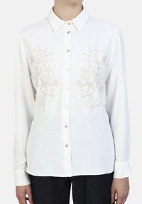 White long-sleeve shirt with a button-up front, featuring beige floral embroidery on the chest. Soft fabric with a classic collar and cuffs.