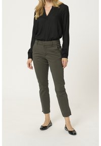 Blouse noire à col en V avec des manches longues, associée à un pantalon slim-fit vert olive et des ballerines noires avec des accents en nœud.