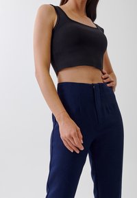 Svart avkortad tanktop med fyrkantig halsringning, kombinerad med högmidjade skräddarsydda byxor i marinblått med framfåll och en diskret dragkedja.