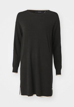 Robe pull noire à manches longues avec des accents côtelés de couleur crème au niveau du col et de l'ourlet. Présente des fentes sur les côtés pour faciliter les mouvements.