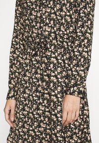 Robe noire à fleurs avec des fleurs roses et crème, dotée de manches longues, d'un devant boutonné et d'une taille à cordon pour un ajustement modulable.