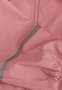 Rosa vattentålig tyg med en slät textur, som har en silverreflekterande rand och rynkdetalj längs nederkanten.