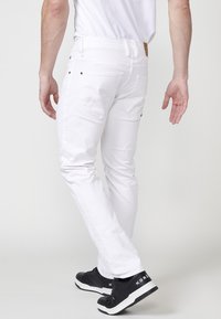 Pantalones vaqueros blancos de denim con un corte ajustado, que cuentan con dos bolsillos traseros, detalles de costura sutiles y combinados con zapatillas deportivas negras.