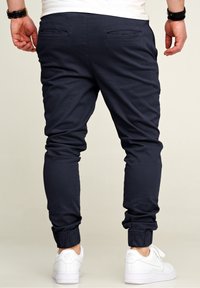 Marineblaue Jogginghosen mit elastischen Bündchen und zwei hinteren Taschen. Hergestellt aus einem glatten Stoff und kombiniert mit weißen Sneakers.